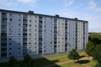 Sanierter Wohnblock in hellen Blautönen, Brüstungen Loggien mittelblau. Flachdach, 9 Etagen. Davor Grünfläche mit Weg und Bäumen. Sanierter Wohnblock in hellen Blautönen, Brüstungen Loggien mittelblau. Flachdach, 9 Etagen. Davor Grünfläche mit Weg und Bäumen.