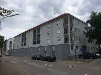 Wohnhäuser mit 4 Etagen, Balkone, graue Fassade, an Straße. Autos.
