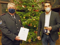 Arno Montada mit seiner Urkunde und mit OB Conradt vor dem Weihnachtsbaum im Rathausfestsaal
