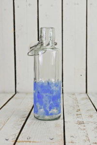 geöffnete Glasflasche mit blauen Herzen vor hölzernem Hintergrund