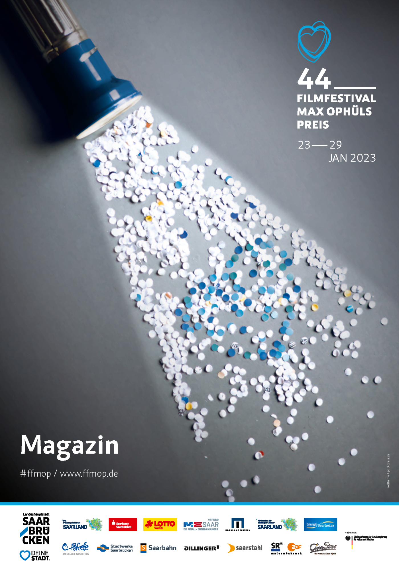 Titelseite Magazin: Blaues Konfettiherz auf weißem Konfetti, das von einer Taschenlampe angestrahlt wird