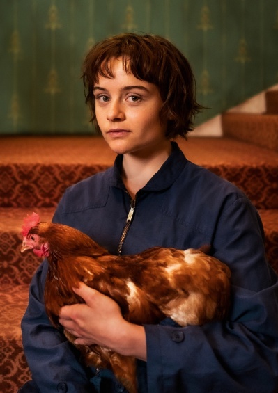 Junge Frau steht vor einer Treppe und hat einen braunen Hahn auf dem Arm
