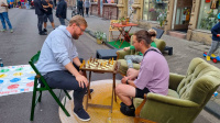 Zwei Männer spielen Schach auf den Sommerstraßen. Neben ihnen ist ein Twister-Spiel zu sehen.