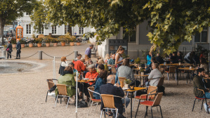 Außenansicht Café am Schloss: Tische mit Gästen unter großen Baum 