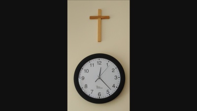 Eine Wand, an der ein Jesuskreuz hängt, darunter hängt eine Uhr