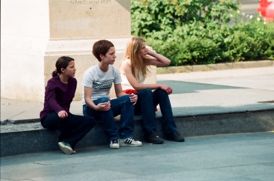 3 Teenies sitzen auf einer Bordsteinkante und schauen alle nach links