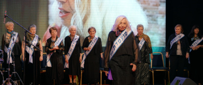 Eine Gruppe älterer Damen stehen auf einer Bühne, alle tragen eine Binde mit hebräischen Schriftzeichen