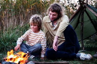 Ein Junge und ein Mann sitzen vor einem Lagerfeuer und Zelt