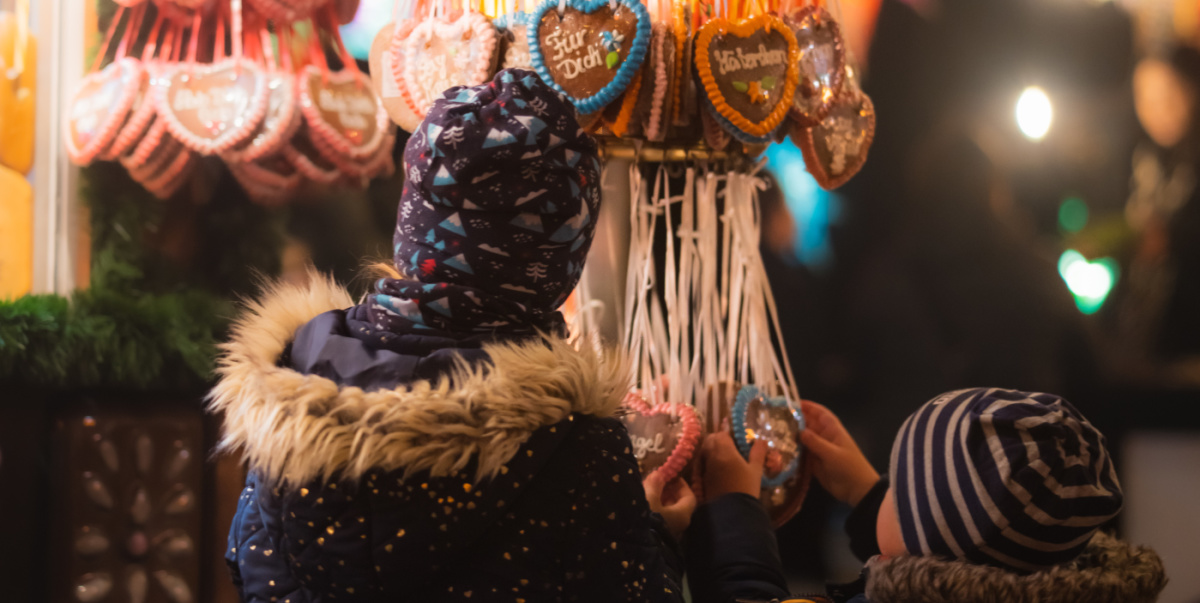 Zwei Kinder von hinten mit Mütze nund Jacken,  vor dem Weihnachtsmarktstand bei der Auswahl von Lebkuchenherzen