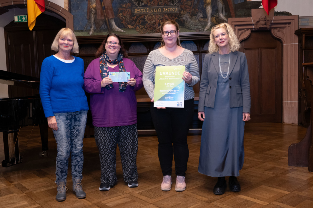 Preisübergabe des vierten Platzes an die Grundschule Hohe Wacht. Zu sehen sind zwei Betreuerinnen welche die Urkunde halten, sowie zwei Jurymitglieder.