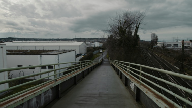 Eine verlassene Fußgängerbrücke, die zwischen einem Industriegebiet und Bahngleisen verläuft.