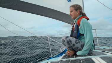 Ein Mädchen sitzt im Schneidersitz auf einem Segelboot und blickt auf's Meer hinaus.