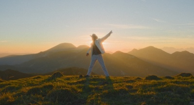 Ein Mann in Cowboy-Outfit steht auf einem Berg bei Sonnenuntergang.