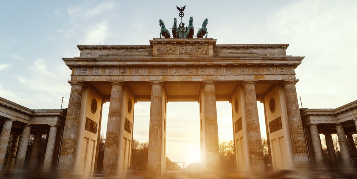 Das Brandenburger Tor in Berlin: Ein helles Steintor mit mehreren Säulen sowie Kutscher und Pferden