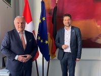 Antrittsbesuch des Schweizer Generalkonsuls Dr. Erik Jakob Zwei Personen stehen vor Flaggenstangen, im Hintergrund sind eine weiße Wand mit Bildern zu erkennen