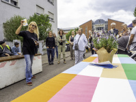 Eine Frau hält einen Zettel in die Luft und redet mit der umherstehenden Gruppe von Menschen