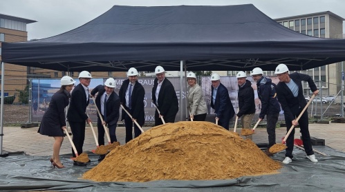 Eine Gruppe Menschen in Anzügen mit Spaten in den Händen schaufelt einen großen Haufen Sand