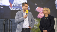 Ein Mann mit Mikrofon und eine Frau stehen auf einer Bühne 