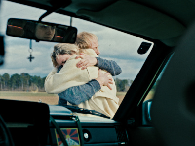 Durch die Windschutzscheibe eines Autos sieht man eine Frau und ein Mann, die sich umarmen. Durch die Windschutzscheibe eines Autos sieht man eine Frau und ein Mann, die sich umarmen.