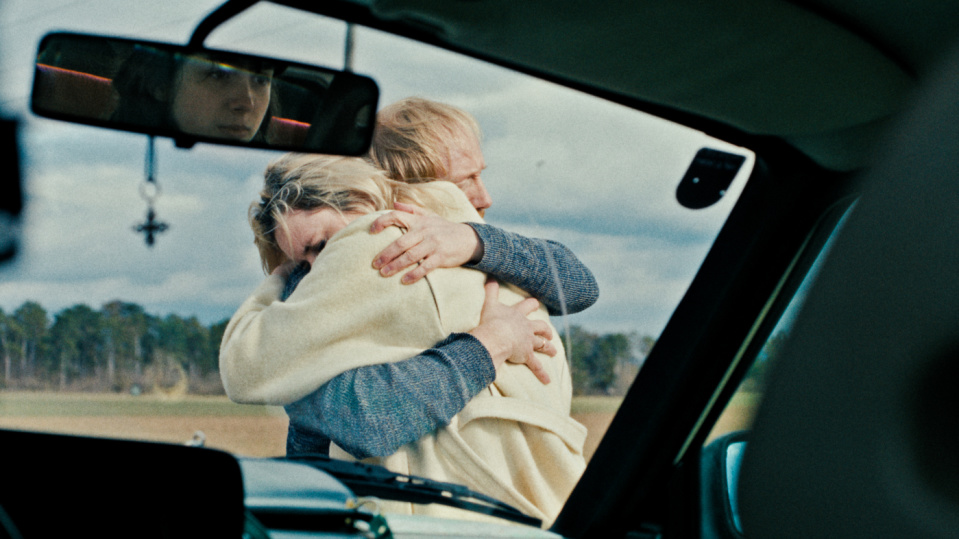 Durch die Windschutzscheibe eines Autos sieht man eine Frau und ein Mann, die sich umarmen. Durch die Windschutzscheibe eines Autos sieht man eine Frau und ein Mann, die sich umarmen.