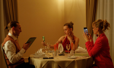 Babystar Still Zwei Frauen und ein Mann sitzen an einem gedeckten Tisch. Die beiden Frauen machen Fotos, der Mann hält eine Speisekarte in der Hand.