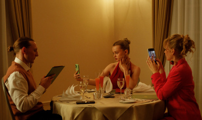 Babystar Still Zwei Frauen und ein Mann sitzen an einem gedeckten Tisch. Die beiden Frauen machen Fotos, der Mann hält eine Speisekarte in der Hand.