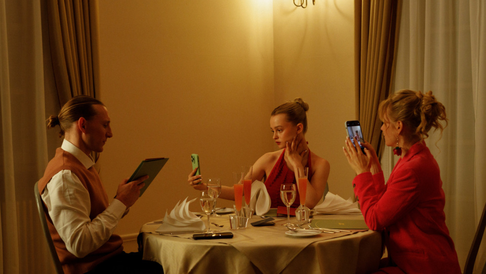 Zwei Frauen und ein Mann sitzen an einem gedeckten Tisch. Die beiden Frauen machen Fotos, der Mann hält eine Speisekarte in der Hand. Zwei Frauen und ein Mann sitzen an einem gedeckten Tisch. Die beiden Frauen machen Fotos, der Mann hält eine Speisekarte in der Hand.