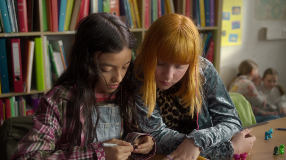 Zwei Mädchen sitzen gemeinsam an einem Tisch und betrachten ein Heft, das vor ihnen liegt. Zwei Mädchen sitzen gemeinsam an einem Tisch und betrachten ein Heft, das vor ihnen liegt.