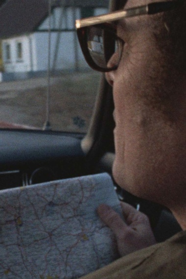 Ein Mann auf dem Beifahrersitz eines Autos hält eine Straßenkarte vor sich in der Hand und schaut aus der Windschutzscheibe des Autos auf die Straße.