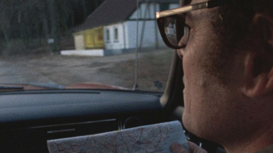 Ein Mann auf dem Beifahrersitz eines Autos hält eine Straßenkarte vor sich in der Hand und schaut aus der Windschutzscheibe des Autos auf die Straße.