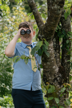 Ein Junge und eine ältere Frau schauen im Garten durch Ferngläser bzw. Lupen neben einem Baum.
