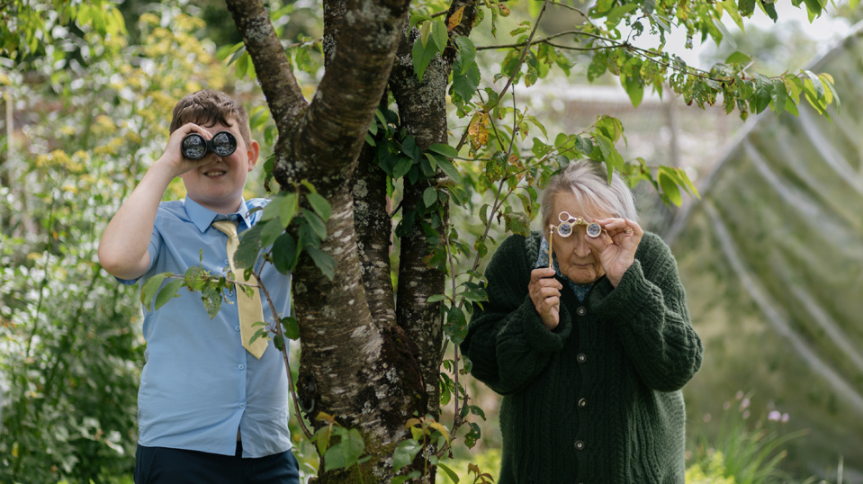 Ein Junge und eine ältere Frau schauen im Garten durch Ferngläser bzw. Lupen neben einem Baum. Ein Junge und eine ältere Frau schauen im Garten durch Ferngläser bzw. Lupen neben einem Baum.
