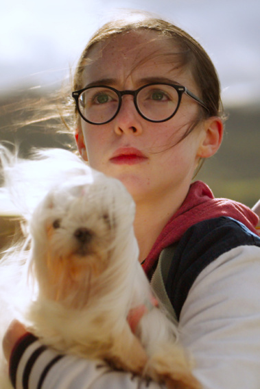 Glitch - Meine Freundin aus einer anderen Dimension Zwei Kinder stehen draußen; eines hält einen kleinen weißen Hund, das andere macht eine verspielte Handbewegung.