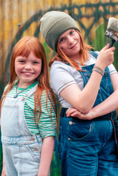 Zwei Kinder mit roten Haaren stehen vor einer bunt besprühten Wand.