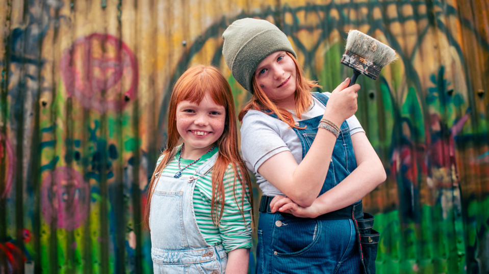 Zwei Kinder mit roten Haaren stehen vor einer bunt besprühten Wand. Zwei Kinder mit roten Haaren stehen vor einer bunt besprühten Wand.