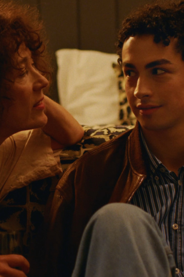 BACKSTAGE Eine Frau und ein Mann sitzen nebeneinander vor einem Bett und unterhalten sich.