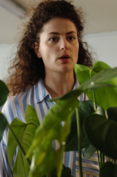 ONKRAUT Eine braunhaarige Frau steht vor einer Monstera-Pflanze.