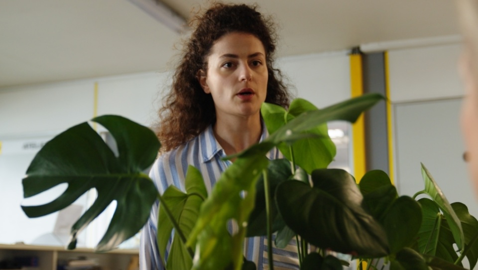 Eine braunhaarige Frau steht vor einer Monstera-Pflanze. Eine braunhaarige Frau steht vor einer Monstera-Pflanze.