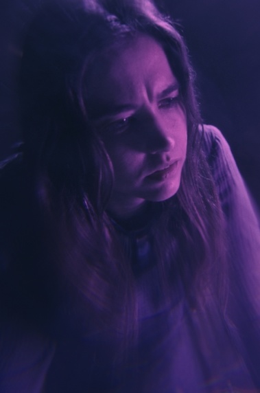 DAEMONICON Eine Frau befindet sich in einem in violettes Licht getauchten Raum.