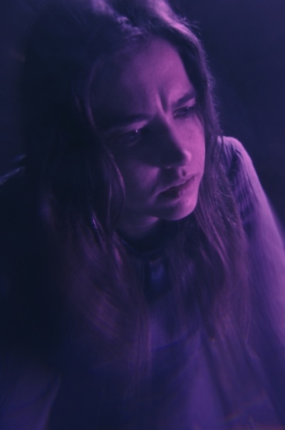 DAEMONICON Eine Frau befindet sich in einem in violettes Licht getauchten Raum.