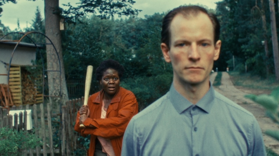 Im Vordergrund steht ein Mann, im Hintergrund bewegt sich eine Frau mit Baseballschläger in der Hand auf ihn zu. Im Vordergrund steht ein Mann, im Hintergrund bewegt sich eine Frau mit Baseballschläger in der Hand auf ihn zu.