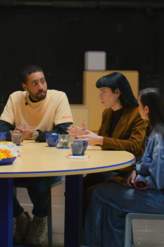 Sechs Personen sitzen in einem büroartigen Raum an einem runden Tisch zusammen.