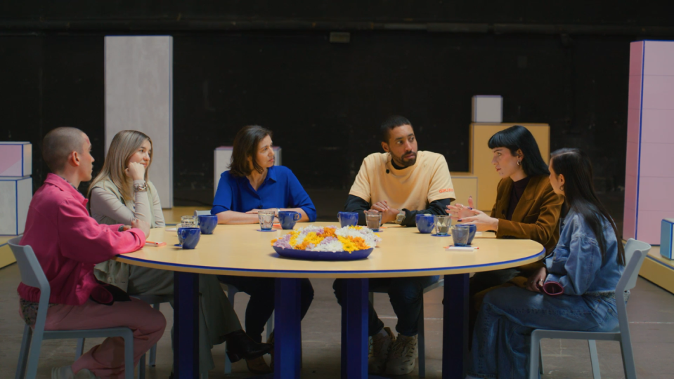 Sechs Personen sitzen in einem büroartigen Raum an einem runden Tisch zusammen.