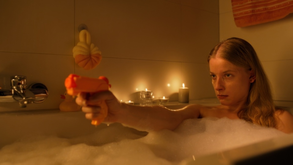 Eine Frau sitzt in der Badewanne. Sie hält eine Plastikpistole in den Händen und zielt damit vor sich. Eine Frau sitzt in der Badewanne. Sie hält eine Plastikpistole in den Händen und zielt damit vor sich.