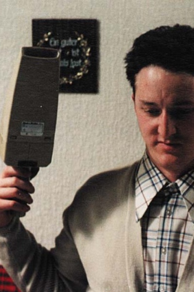 Einer junger Mann schaut vor sich und hält in seiner rechten Hand einen Handstaubsauger.