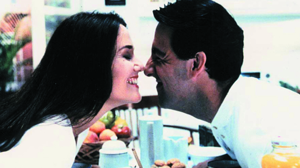 Eine Frau und ein Mann neigen sich zueinander über einen gedeckten Frühstückstisch.