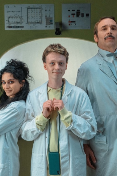 SCHLECHTE MENSCHEN Eine Frau, einer junger und ein älterer Mann stehen zusammen und schauen in die Kamera. Sie tragen weiße Arztkittel.