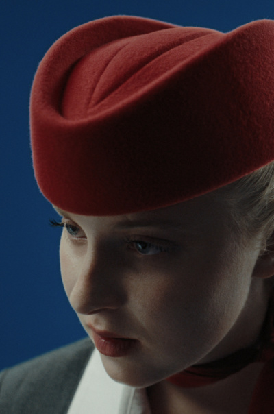 OUT OF THE BLUE Eine blonde Frau trägt eine rote Kopfbedeckung.