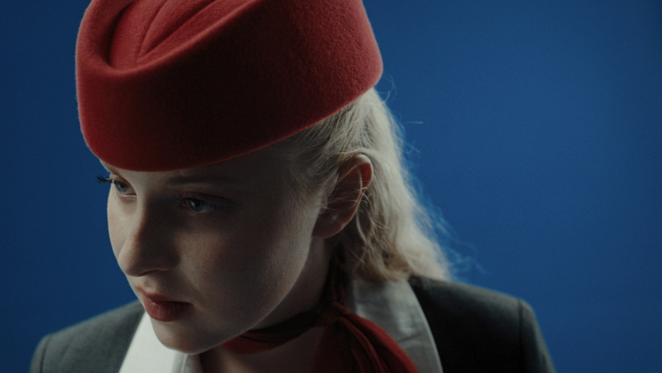 Eine blonde Frau trägt eine rote Kopfbedeckung.