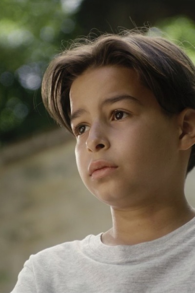 LA PERCÉE Ein kleiner Junge steht draußen vor einer Mauer.